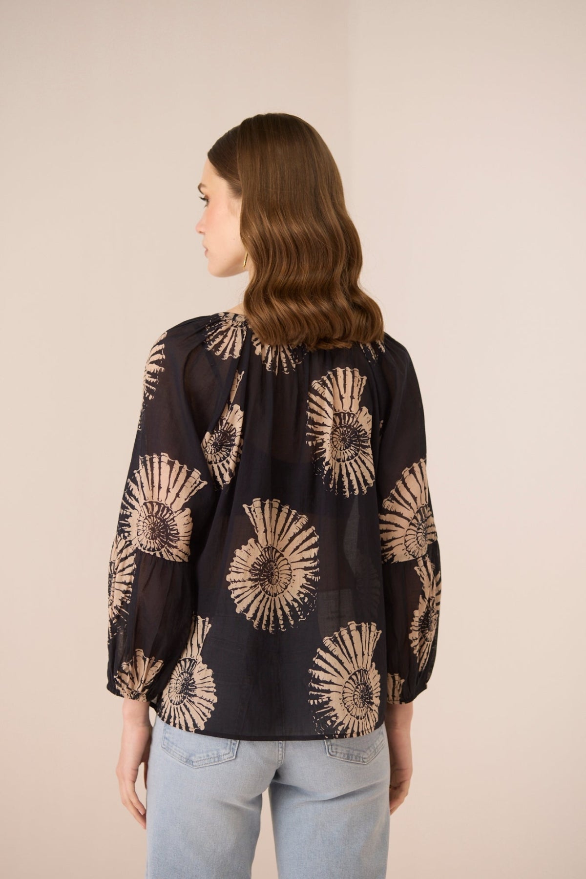 Woman wearing a black blouse with gold floral patterns on a beige background Calling June