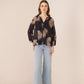 Woman wearing a black patterned blouse and light blue jeans on a beige background Calling June
