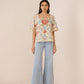 Woman wearing a floral blouse and light blue jeans on a beige background Calling June