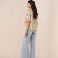 Woman wearing a floral blouse and light blue jeans on a beige background Calling June