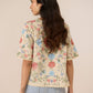 Woman wearing a floral blouse and light blue jeans against a beige background Calling June