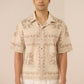 Man wearing a beige patterned shirt and white pants against a plain background Calling June