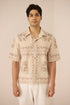 Man wearing a beige patterned shirt and white pants against a plain background Calling June