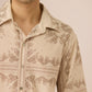 Man wearing a beige patterned shirt against a plain background Calling June