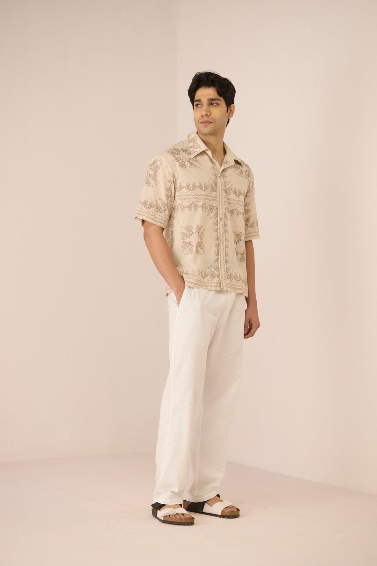 Man wearing a beige patterned shirt and white pants on a beige background Calling June