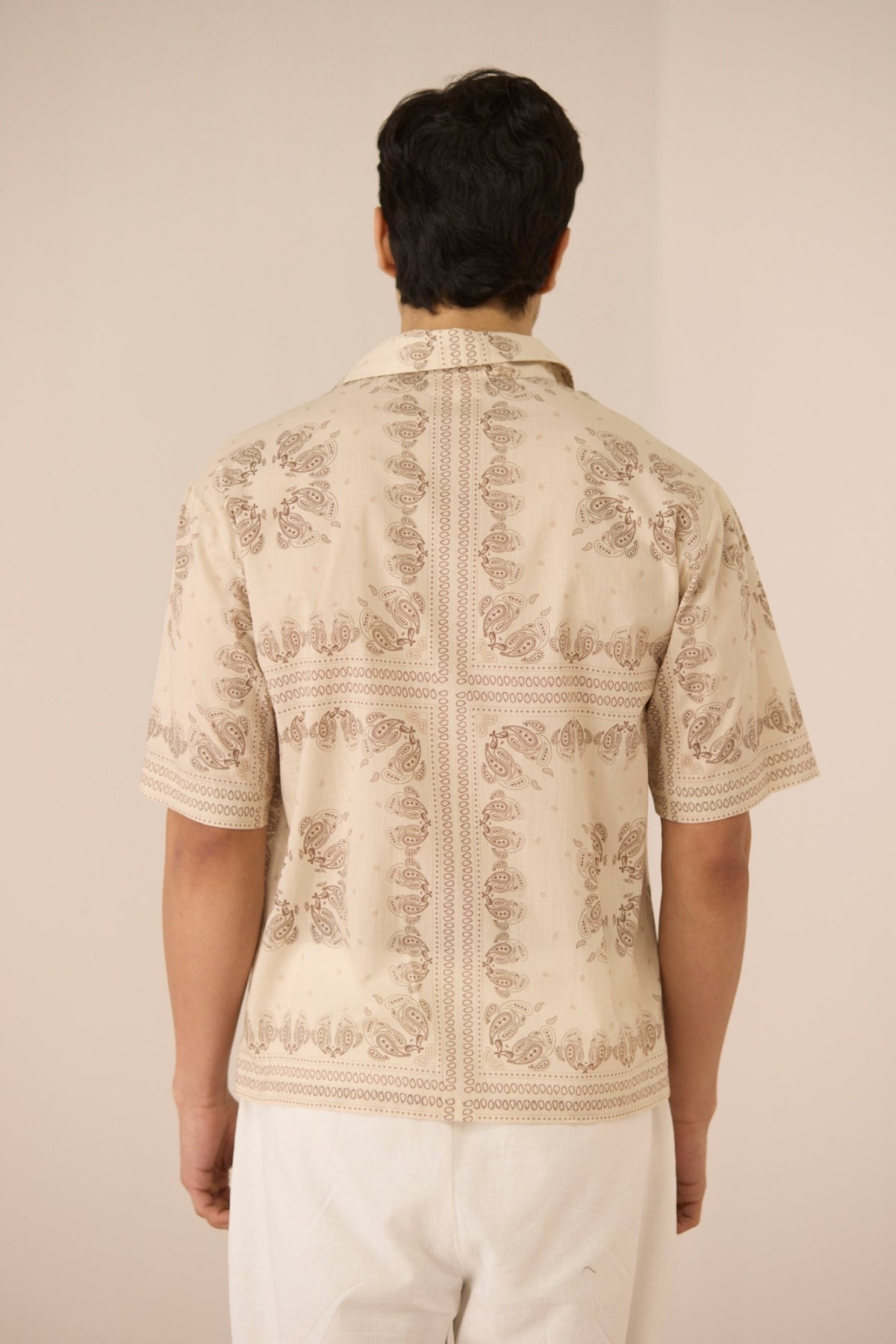Person wearing a cream embroidered shirt with white pants on a plain background Calling June
