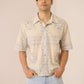 Man wearing a beige patterned shirt and light blue jeans against a beige background Calling June