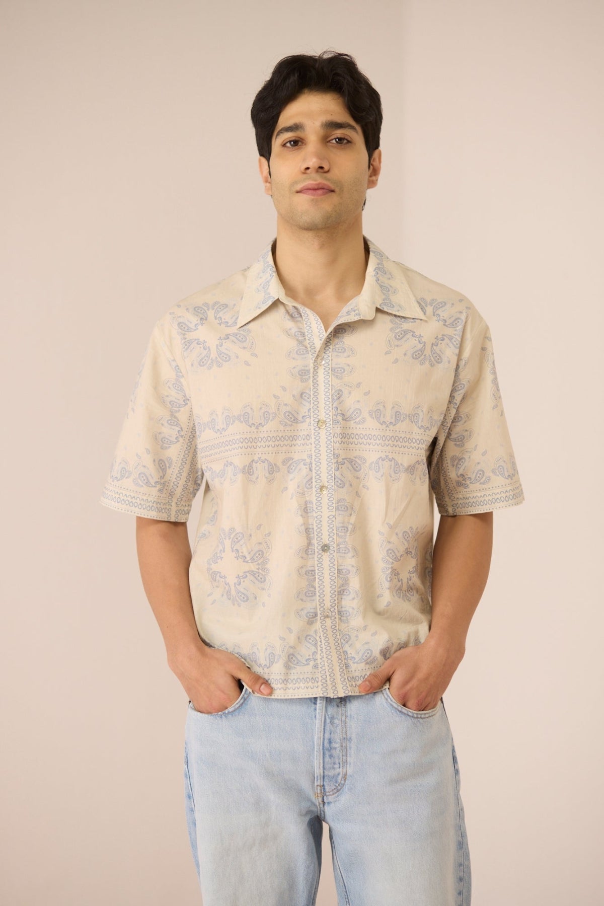 Man wearing a beige patterned shirt and light blue jeans against a beige background Calling June