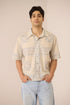 Man wearing a beige patterned shirt and light blue jeans against a beige background Calling June