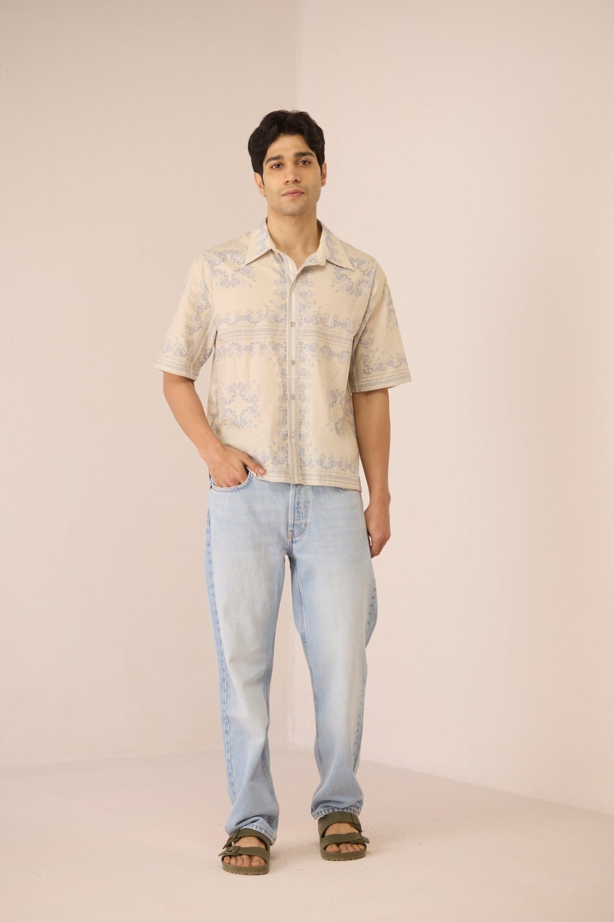 Man wearing a patterned shirt and light blue jeans against a plain background Calling June