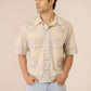 Man wearing a patterned shirt and light blue jeans against a beige background Calling June