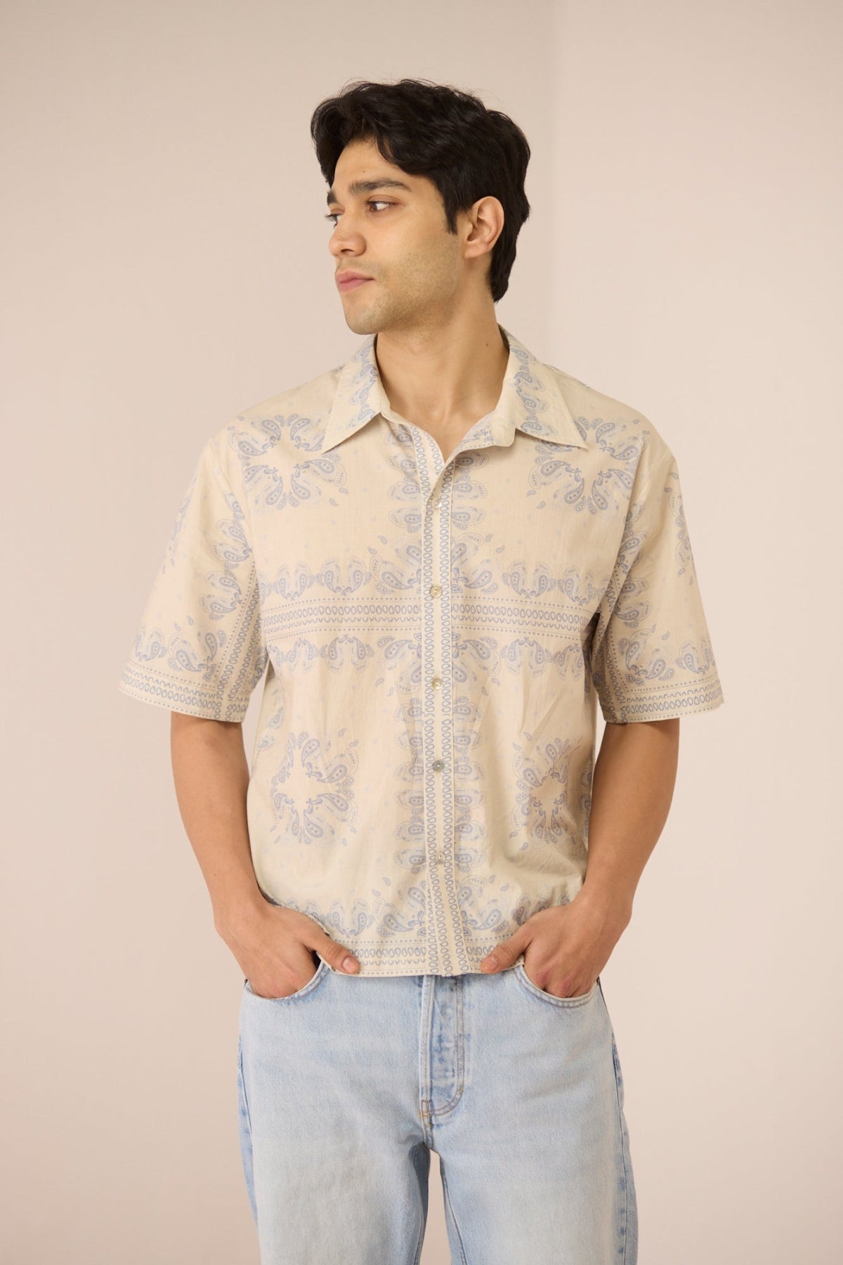 Man wearing a patterned shirt and light blue jeans against a beige background Calling June