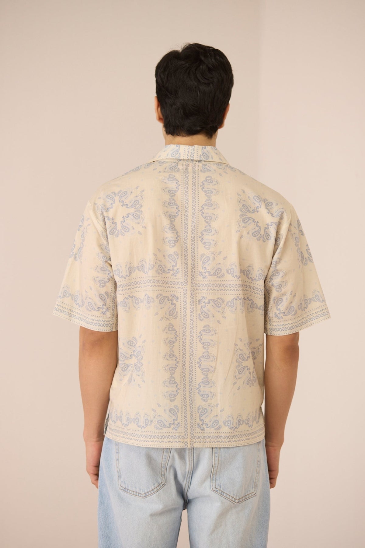Person wearing a beige patterned shirt and light blue jeans against a plain background Calling June