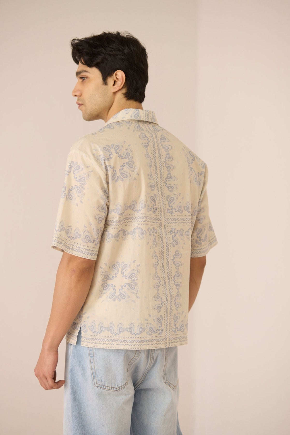Man wearing a patterned beige shirt and light blue jeans against a plain background Calling June