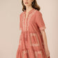 Woman wearing a pink embroidered dress against a beige background Calling June