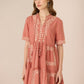 Woman wearing a pink dress with white embroidery on a beige background Calling June
