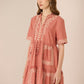 Woman wearing a pink dress with embroidery on a beige background Calling June