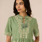 Woman wearing a green dress with floral embroidery against a beige background Calling June