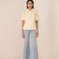 Woman wearing a light yellow blouse with short sleeves and light blue jeans on a beige background Calling June