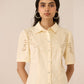 Woman wearing a cream-colored shirt with floral embroidery on a beige background Calling June