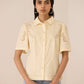 Woman wearing a light yellow embroidered shirt against a beige background Calling June