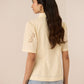 Woman wearing a light yellow polo shirt with floral embroidery on the sleeves against a plain background Calling June