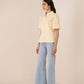 Woman wearing a light yellow blouse and light blue jeans on a beige background Calling June