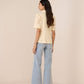 Woman wearing a cream top and light blue jeans on a beige background Calling June