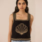 Woman wearing a black sleeveless top with gold embroidery against a beige background Calling June