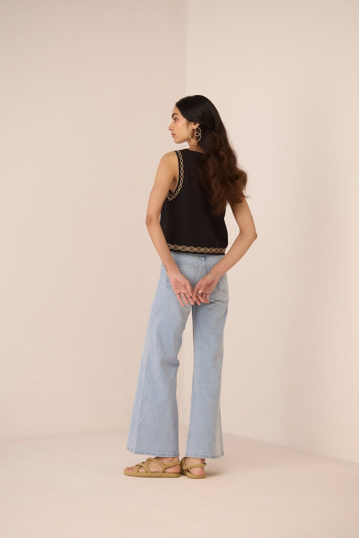 Woman wearing a black sleeveless top with lace details and light blue jeans on a beige background Calling June