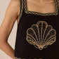 Black top with gold shell design and trim worn by a person Calling June