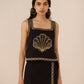 Woman wearing a black dress with gold embroidery on a beige background Calling June