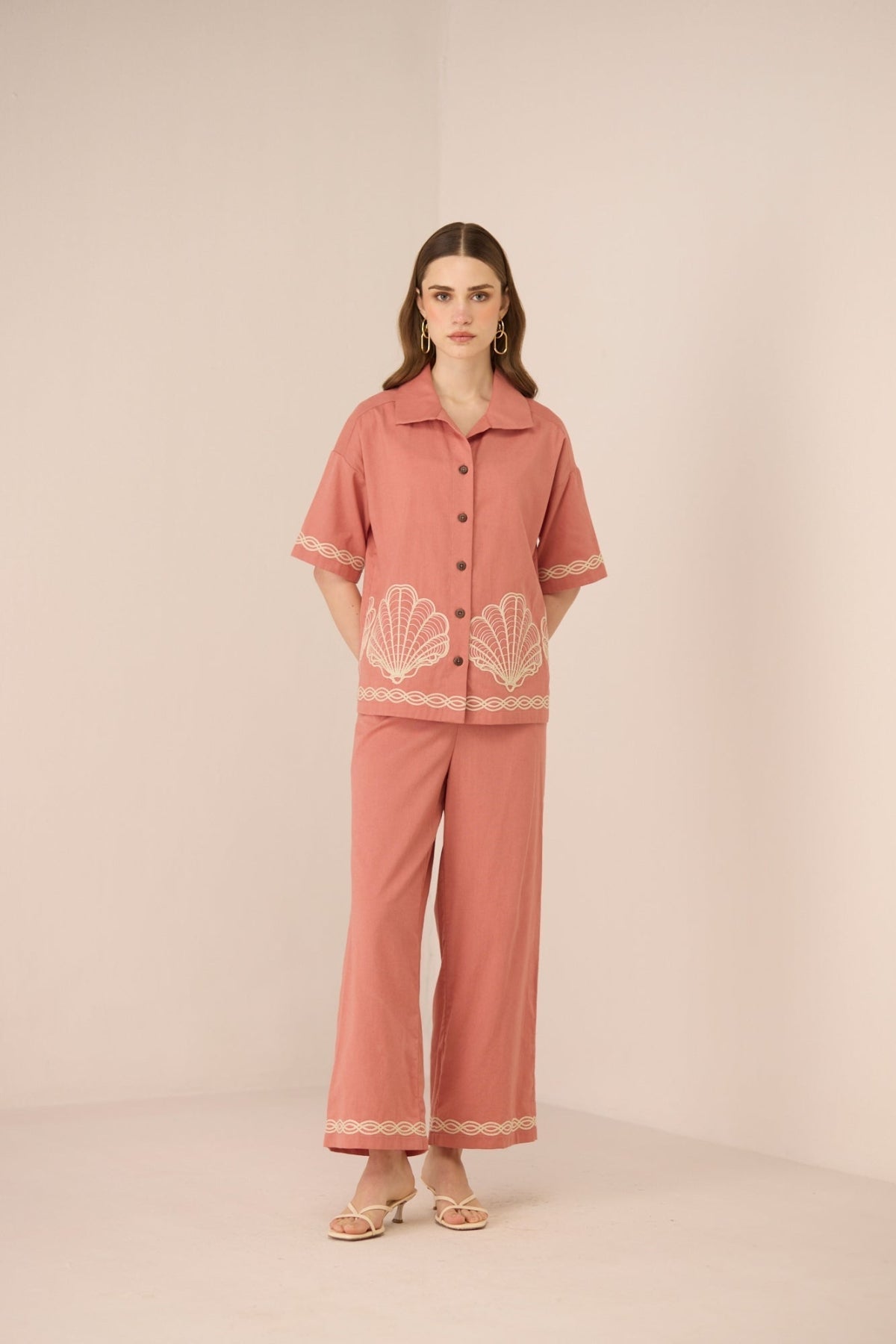 Woman wearing a pink outfit with shell embroidery on a beige background Calling June