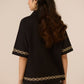 Woman wearing a black blouse with gold embroidery on a beige background Calling June