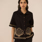 Woman wearing a black top with gold embroidery on a beige background Calling June