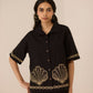 Woman wearing a black blouse with gold embroidery on a beige background Calling June