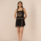 Woman wearing a black dress with gold embroidery against a beige background Calling June