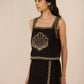 Woman wearing a black dress with gold embroidery against a beige background Calling June