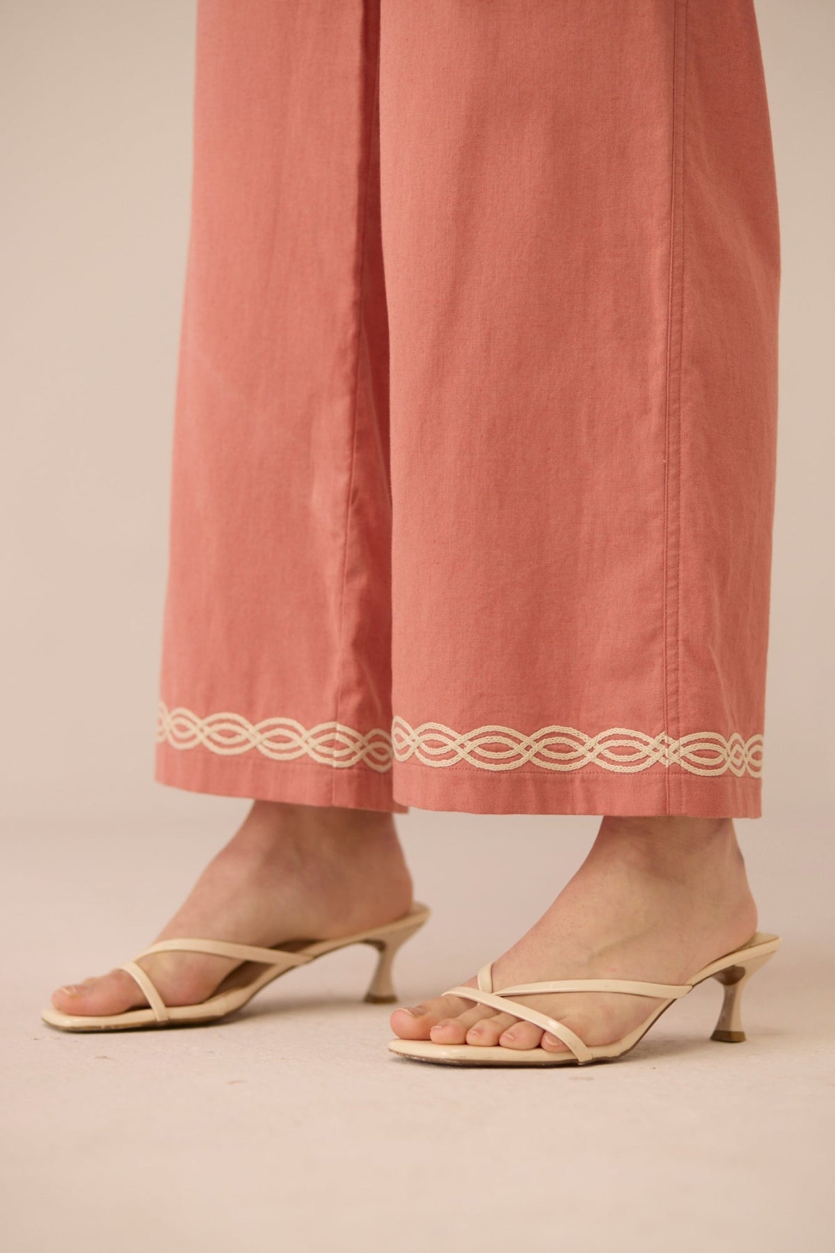 Coral pants with decorative waistband and beige sandals on a neutral background Calling June