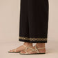 Person wearing black pants with gold embroidery and beige sandals on a beige background Calling June