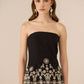 Woman wearing a black strapless top with white embroidery on a beige background Calling June