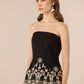 Woman wearing a black strapless top with white lace details on a beige background Calling June