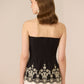 Woman wearing a black strapless top with white embroidery on a beige background Calling June