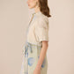 Woman wearing a light-colored dress with a patterned belt against a beige background Calling June
