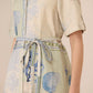 Person wearing a light-colored shirt with a floral pattern and a matching skirt on a neutral background Calling June