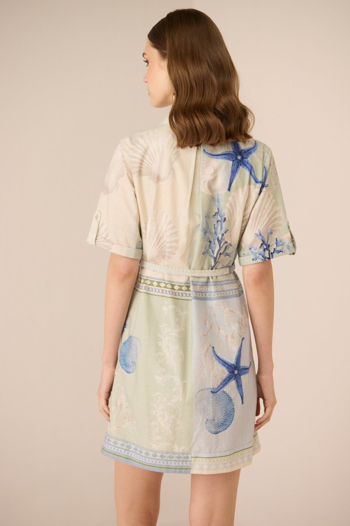 Woman wearing a light-colored dress with blue starfish patterns on a beige background Calling June