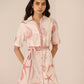 Woman wearing a pink and white dress with shell pattern on a beige background Calling June