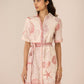 Woman wearing a pink dress with shell pattern against a beige background Calling June