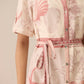 Close-up of a pink and white patterned dress with a belt on a neutral background Calling June