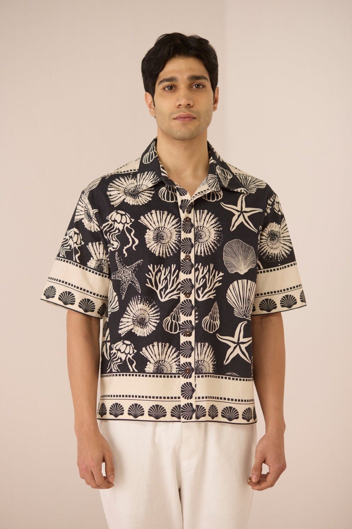 Man wearing a black and white patterned shirt with beige pants on a plain background Calling June